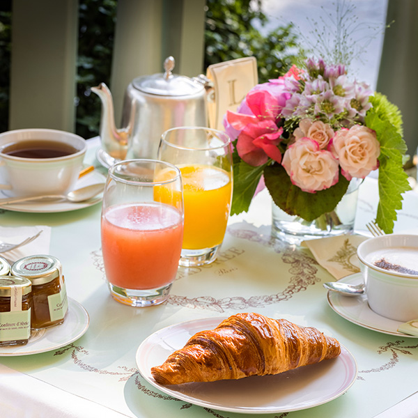 Petit-déjeuner raffiné chez Ladurée Paris, avec croissant, jus frais et thé dans un cadre élégant et fleuri.