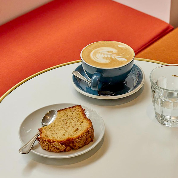 Petit-déjeuner cosy chez Ten Belles à Paris, avec café latte et gâteau maison dans un cadre minimaliste.